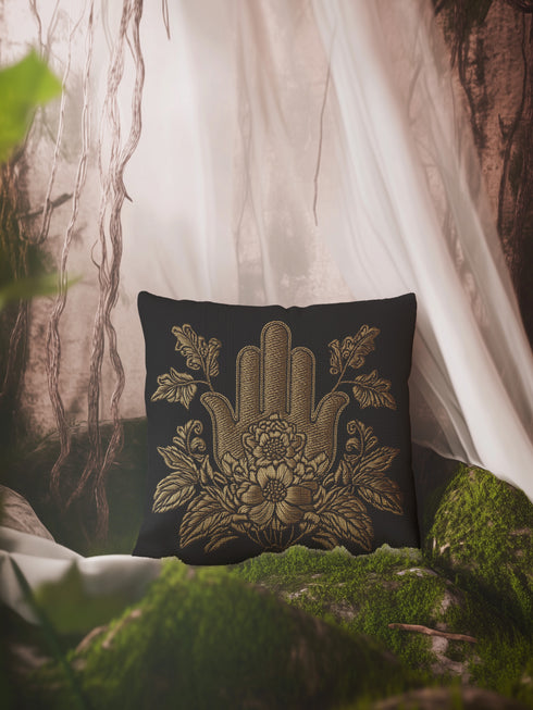 A black woven throw pillow featuring an embroidered gold Hamsa hand surrounded by intricate floral and botanical designs.